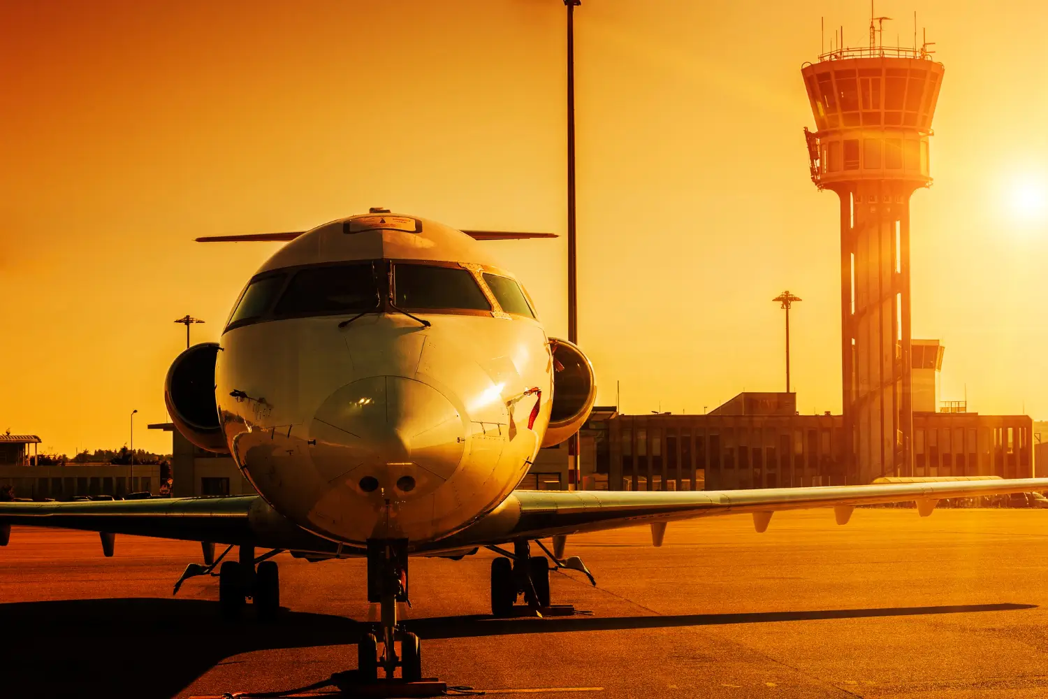 Jato estacionado no pátio de um aeroporto, com a torre de controle ao pôr do sol